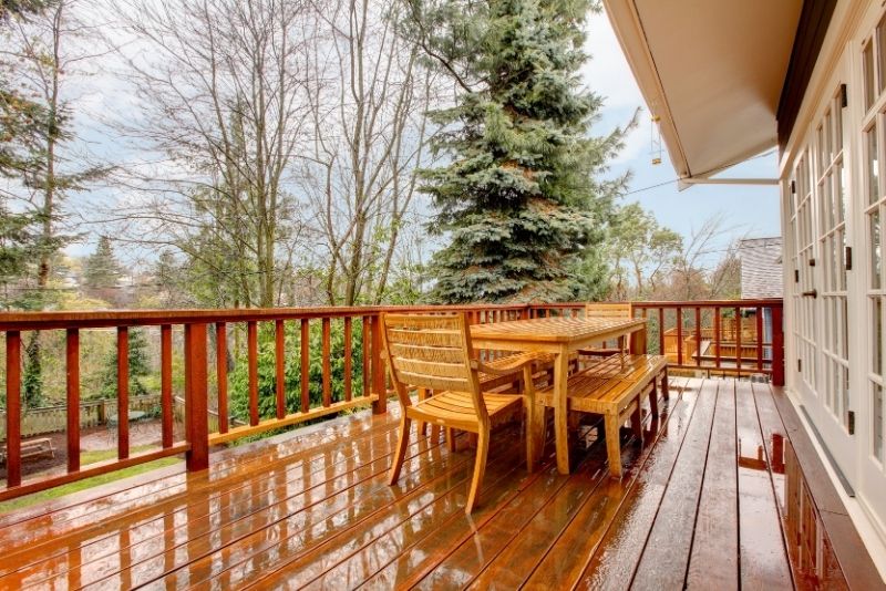 Rain-slicked timber deck with a wooden dining table and bench overlooking the garden