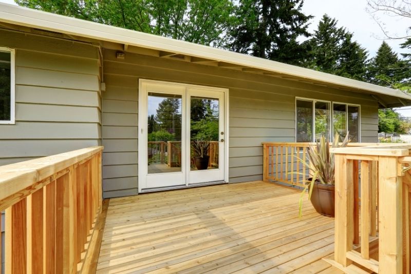 New timber deck with cedar-style railing outside a home's back entrance