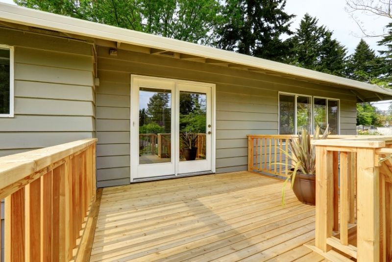 New timber deck with cedar-style railing outside a home's back entrance