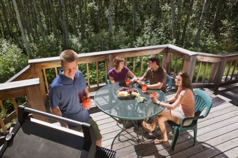 Two couples having drinks around a table on a timber deck in a wooded backyard