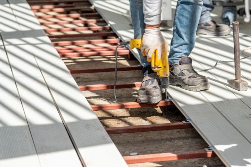 Tradesperson using a drill to install composite decking boards on a frame